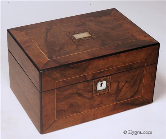Ref: 642JB:  Antique box veneered with  figured walnut, the top and front having a central panel framed by a crossbanding of straight grained walnut and having an inlayed line. There is a mother of pearl escutcheon surrounded a a parquetry inlay in the center of the top. The box opens to a velvet lined lift-out tray. The inside of the lid is lined with lined with satin which is button padded.  The box is edged with ebony and has a working lock and key. Circa 1870.  Enlarge Picture